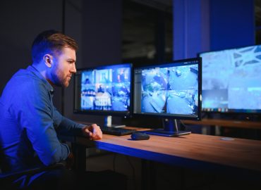 Security operator controls CCTV cameras in office at night.